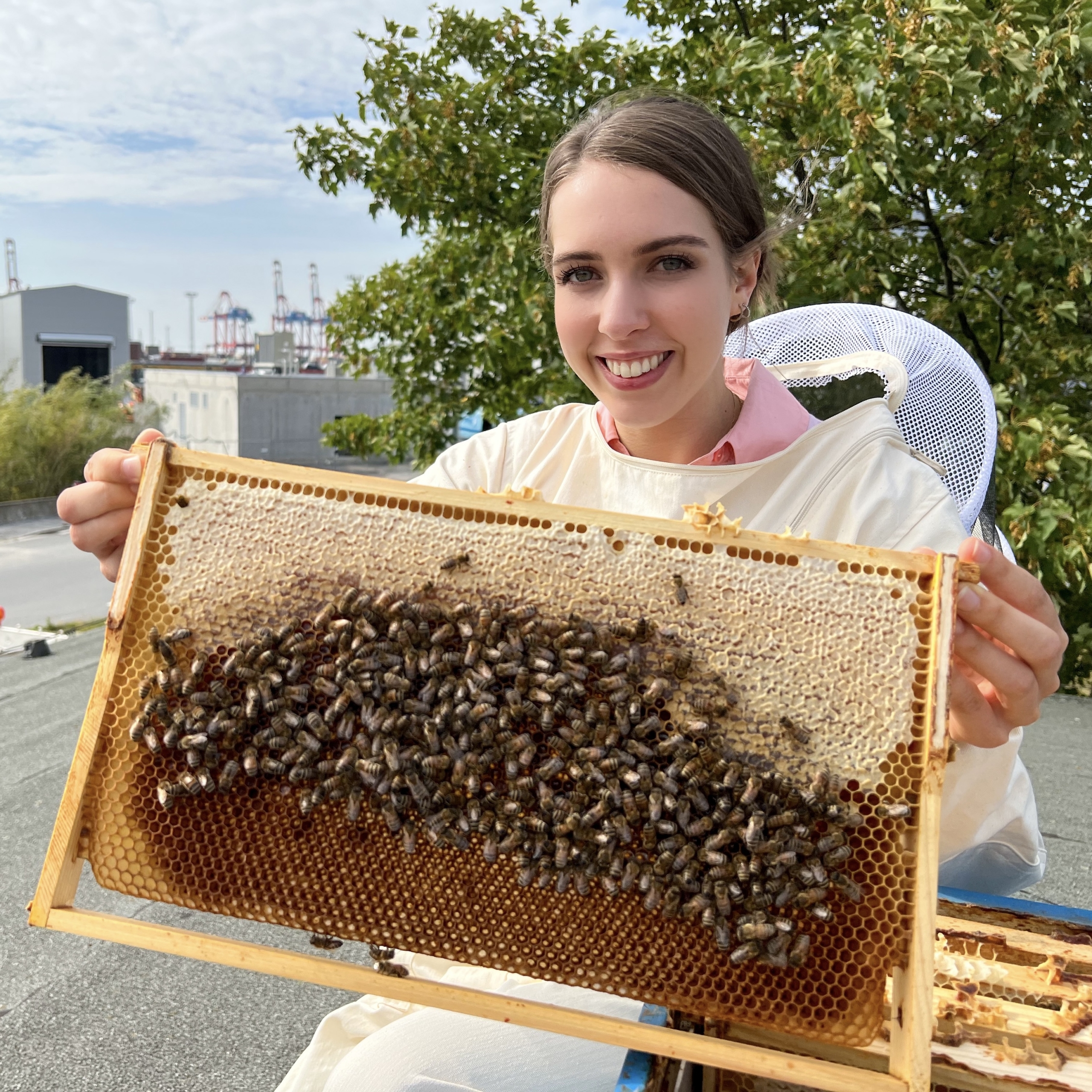 Eine Frau hält eine Bienenwabe mit vielen Bienen darin in den Händen und lächelt